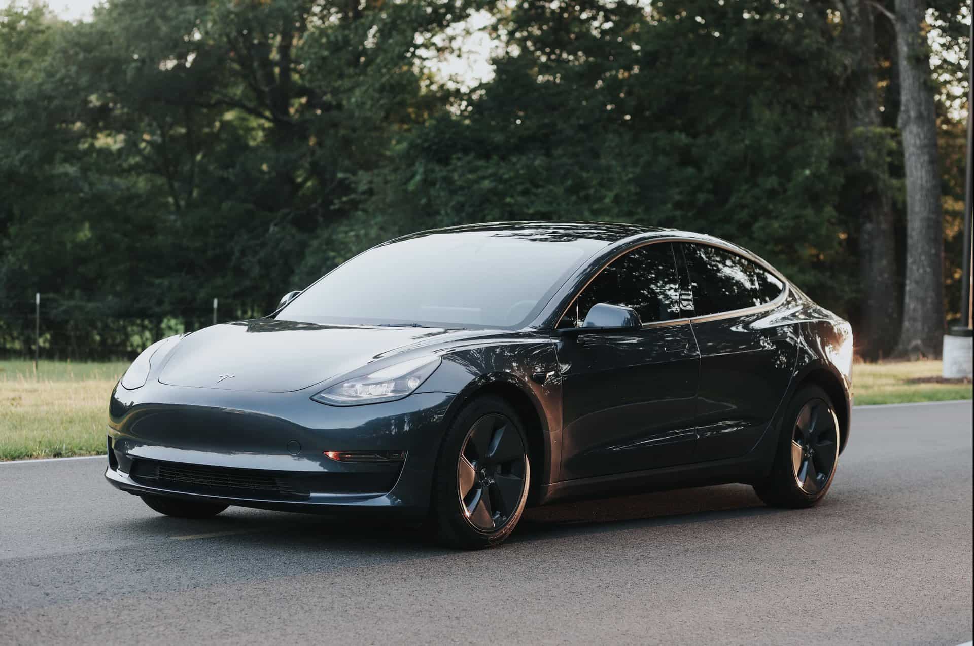 Black electric sedan parked on the side of a road with trees in the background during daylight.