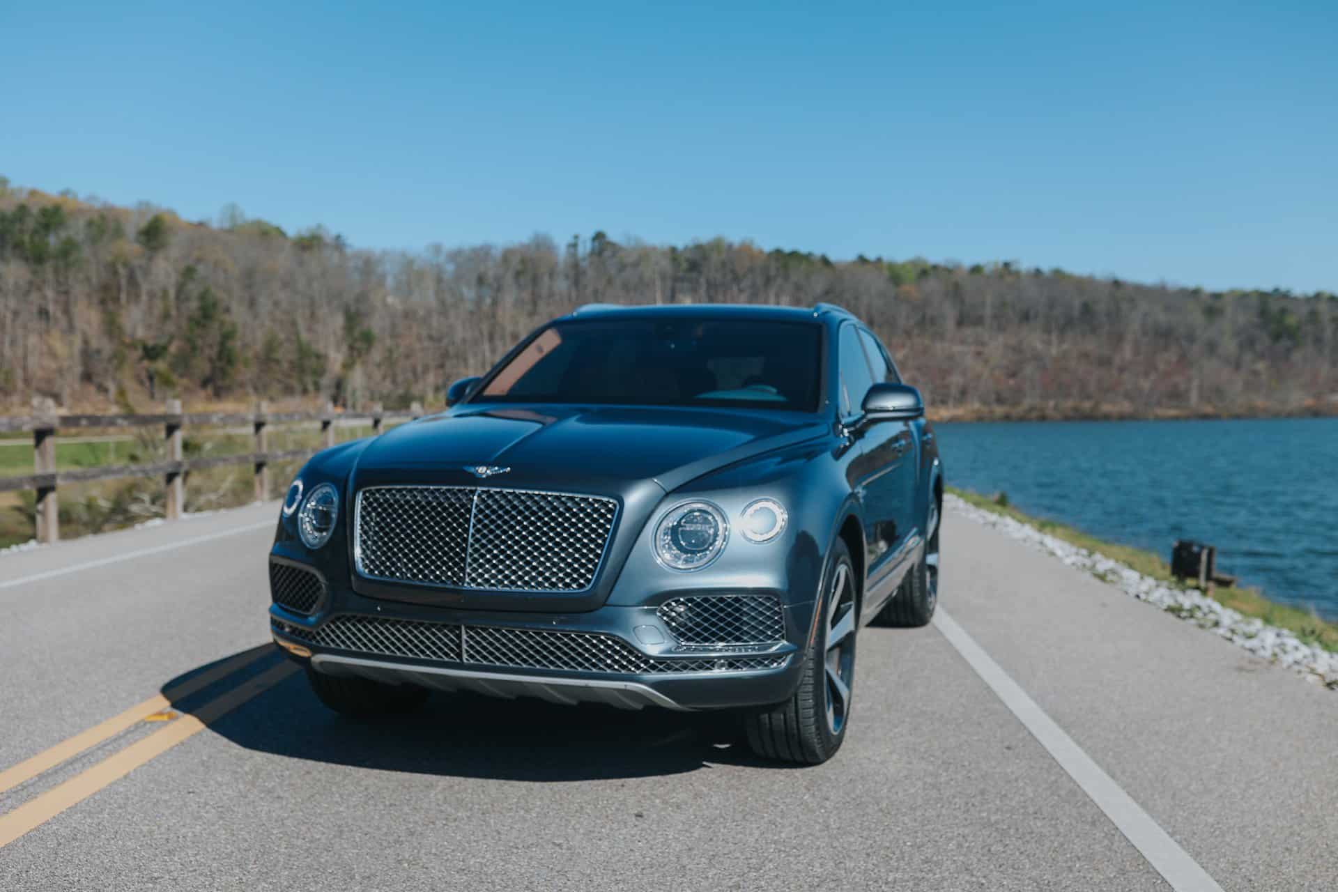 A luxury suv parked on a road next to a body of water on a clear day.