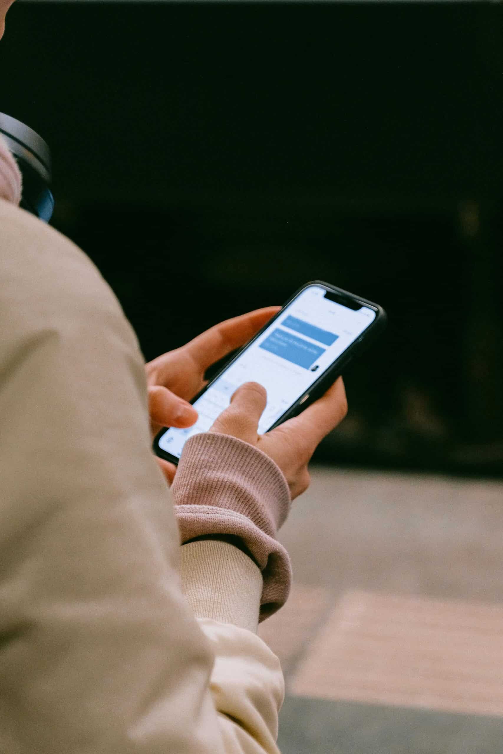 A person holding a smartphone with text on the screen, likely reading or typing a message, while standing on a platform.